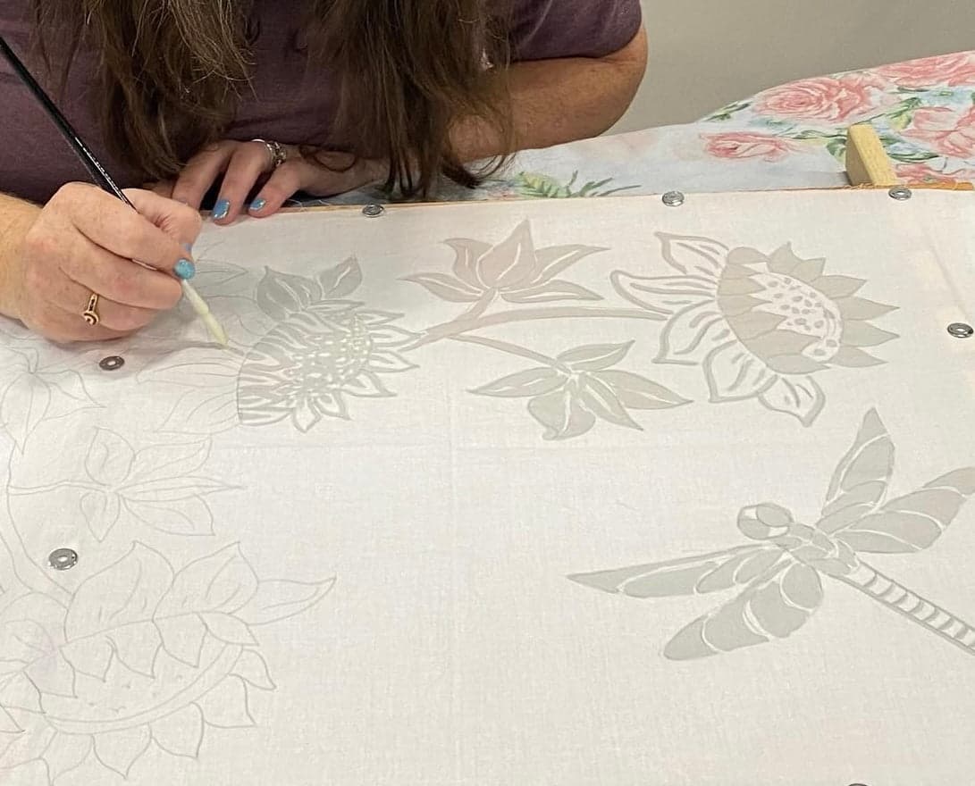 A workshop guest painting a floral and dragonfly batik design onto stretched fabric