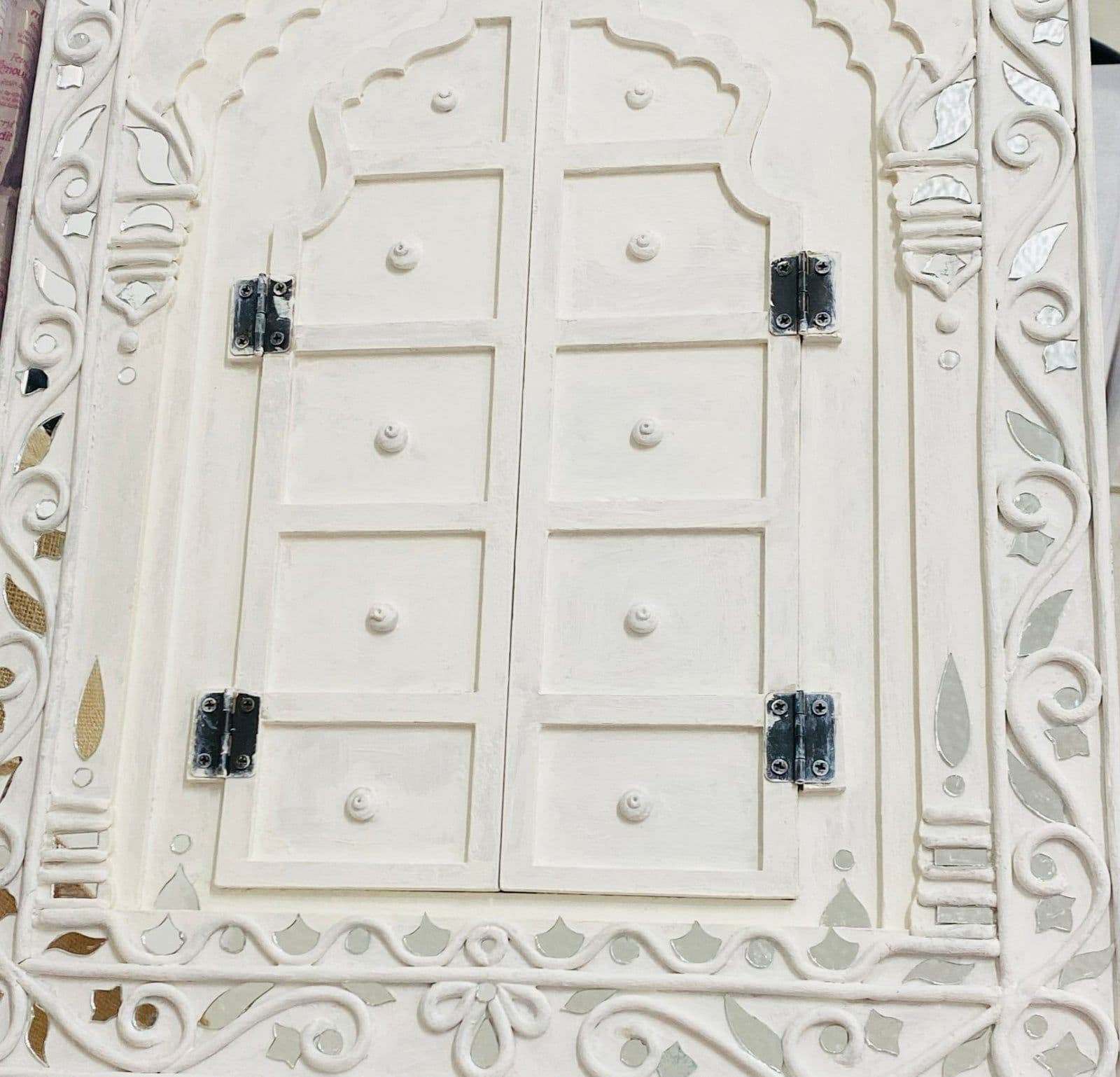 A white Lippan Jharokha frame with hinged doors, decorated with clay patterns and small mirrors